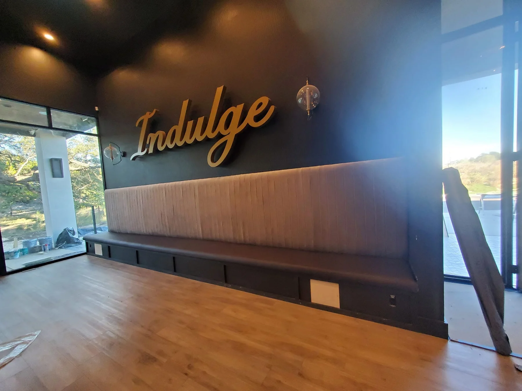 Long channel-tufted tan banquette installed below an Indulge wall sign